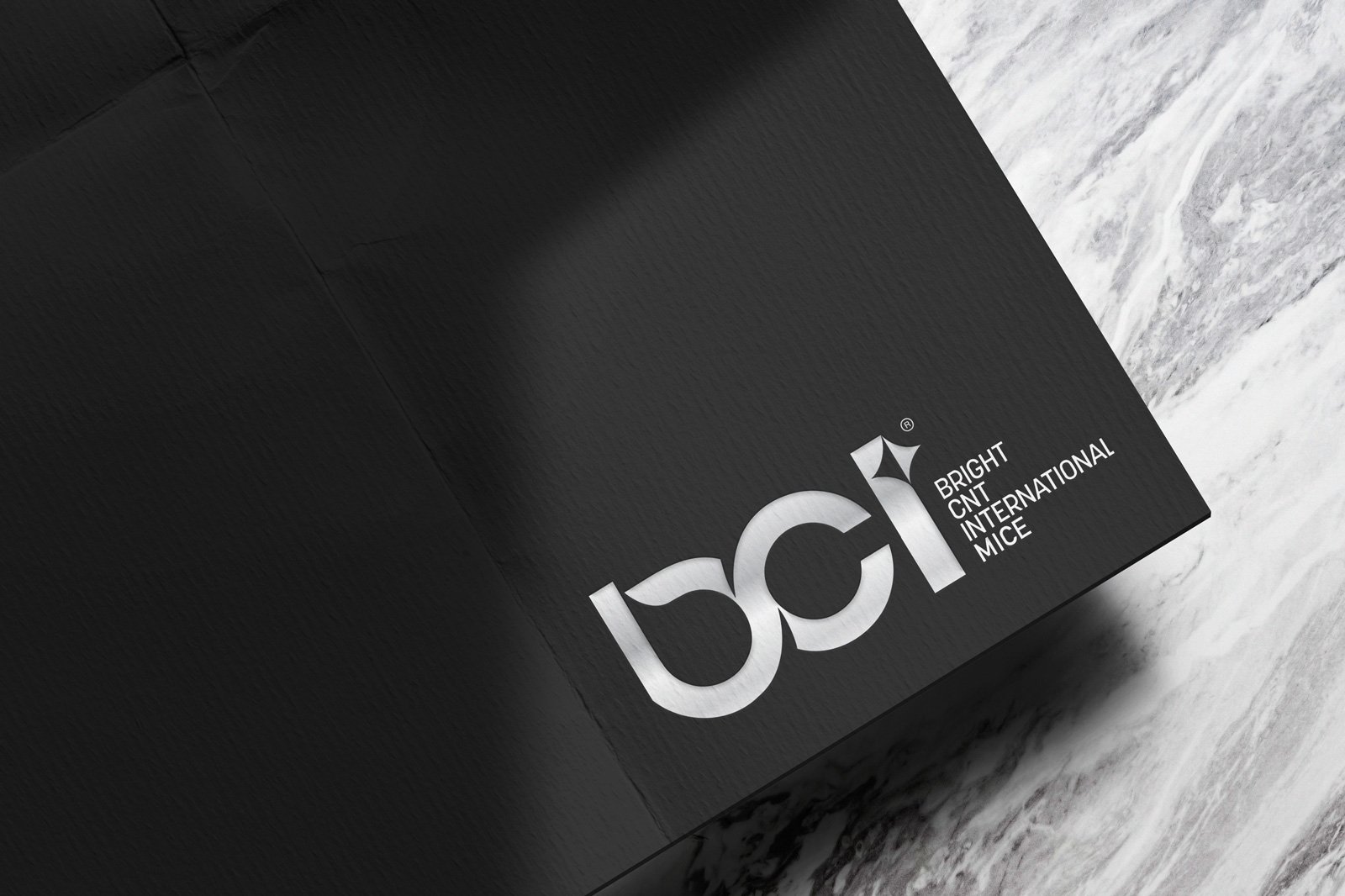 Siyah dokulu kâğıt üzerinde gümüş baskı BCI Bright CNT International MICE logosu, yanında mermer yüzey